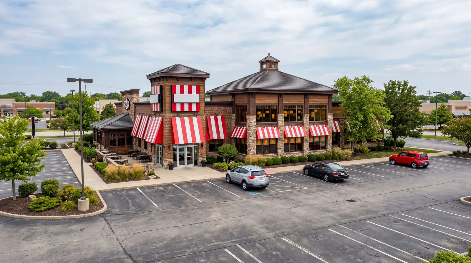 A TGI Friday's-style casual dining restaurant exterior with red and white striped awning, near-empty parking lot at daytime, photorealistic, no text, no watermark, 16:9