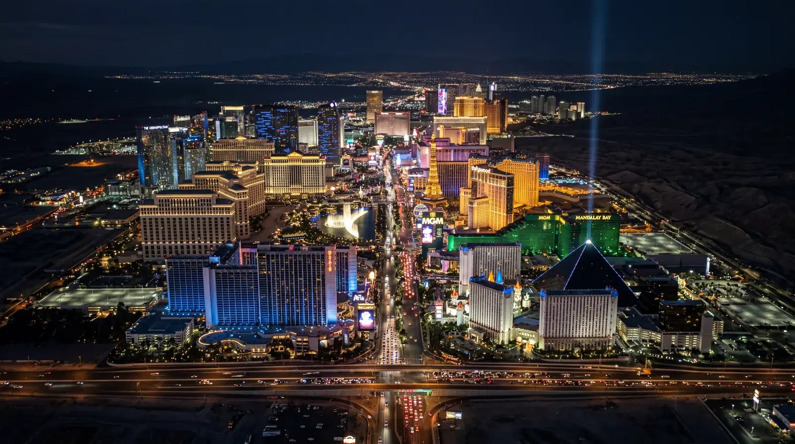 Las Vegas Nevada Strip blazing at night from above, casino towers lit in neon and LED, gridlocked traffic far below, surrounding desert darkness swallowing everything beyond. documentary travel photography, realistic, no text, no watermark, 16:9