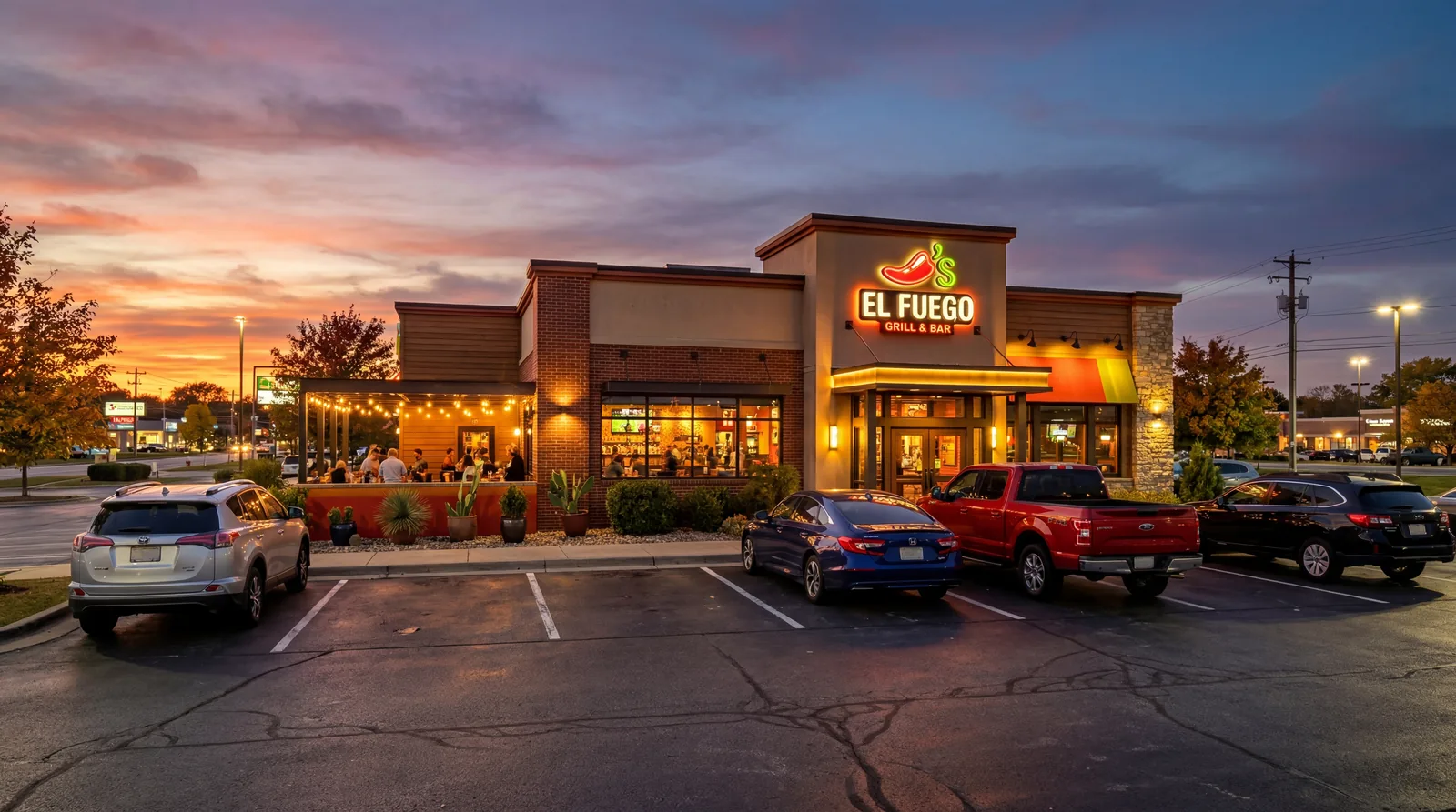 A Chili's-style casual American restaurant exterior at sunset with lit signage, a handful of cars in the parking lot, photorealistic, no text, no watermark, 16:9