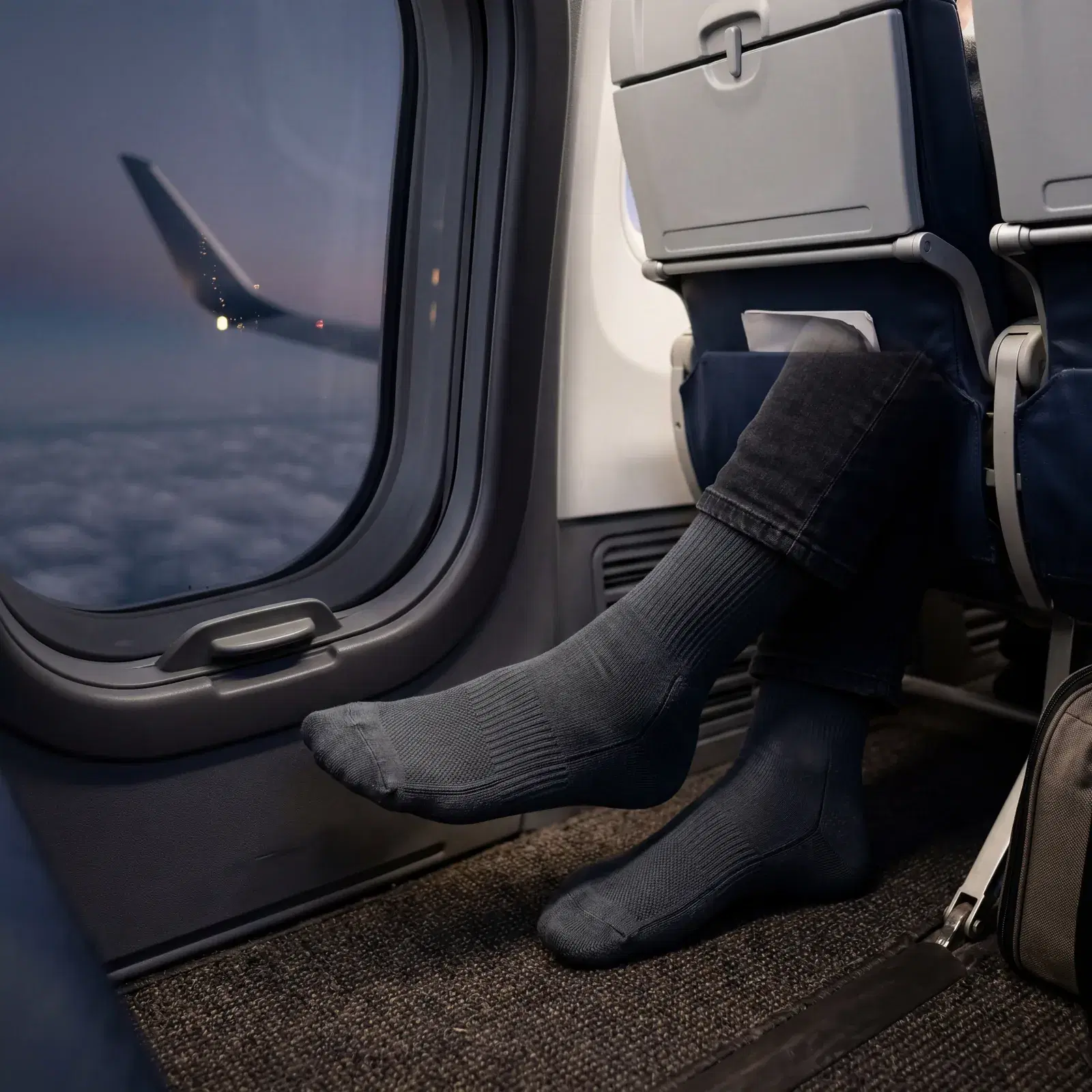 Close-up of compression socks on feet inside airplane cabin, window seat, long-haul flight, photorealistic, editorial travel photography, no text, no watermark, 16:9