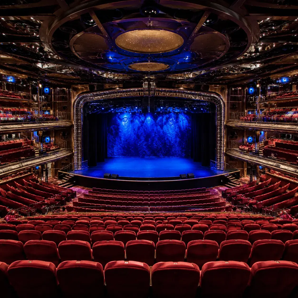 Realistic editorial photo of a cruise ship theater with rows of seats and stage lights before a show, a few passengers e