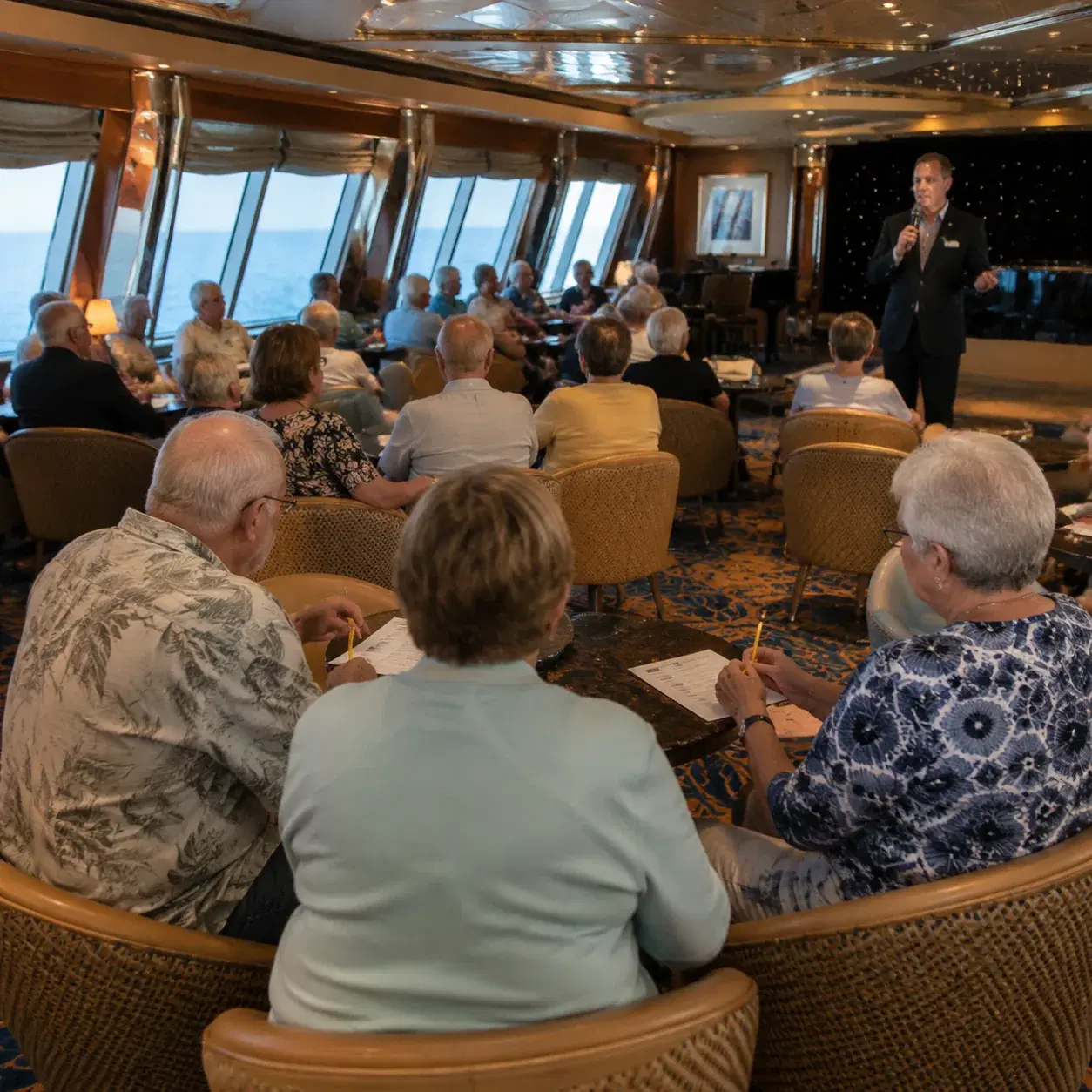 Realistic editorial photo of cruise lounge trivia session with answer sheets, pencils, and small groups at tables, brigh
