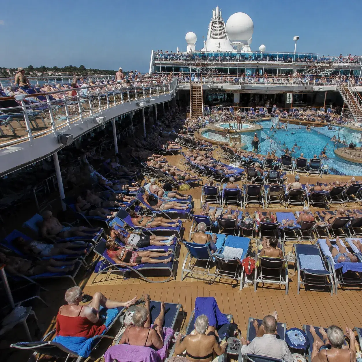 Realistic editorial photo of cruise pool deck game with passengers laughing, towels, and lounge chairs nearby, sunny ene