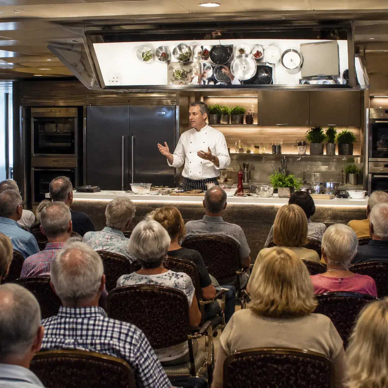 Realistic editorial photo of cruise ship demonstration table with chef utensils, folded napkins, and passengers watching