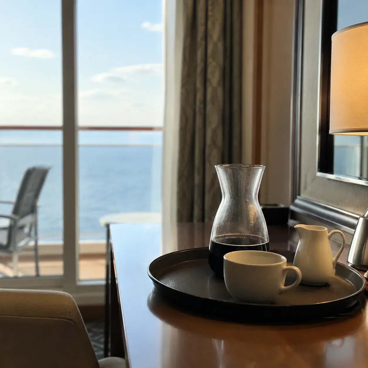 Realistic editorial photo of a cruise cabin breakfast tray with coffee, pastries, and fruit on a small balcony table, mo