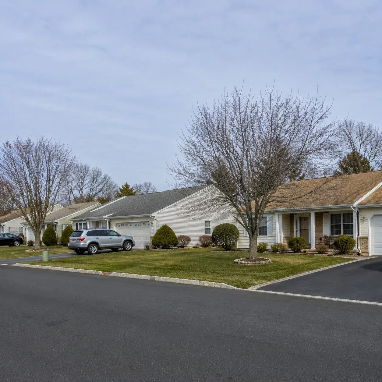Realistic editorial photo of a large Ocean County retirement neighborhood with modest ranch homes, tidy lawns, parked ca