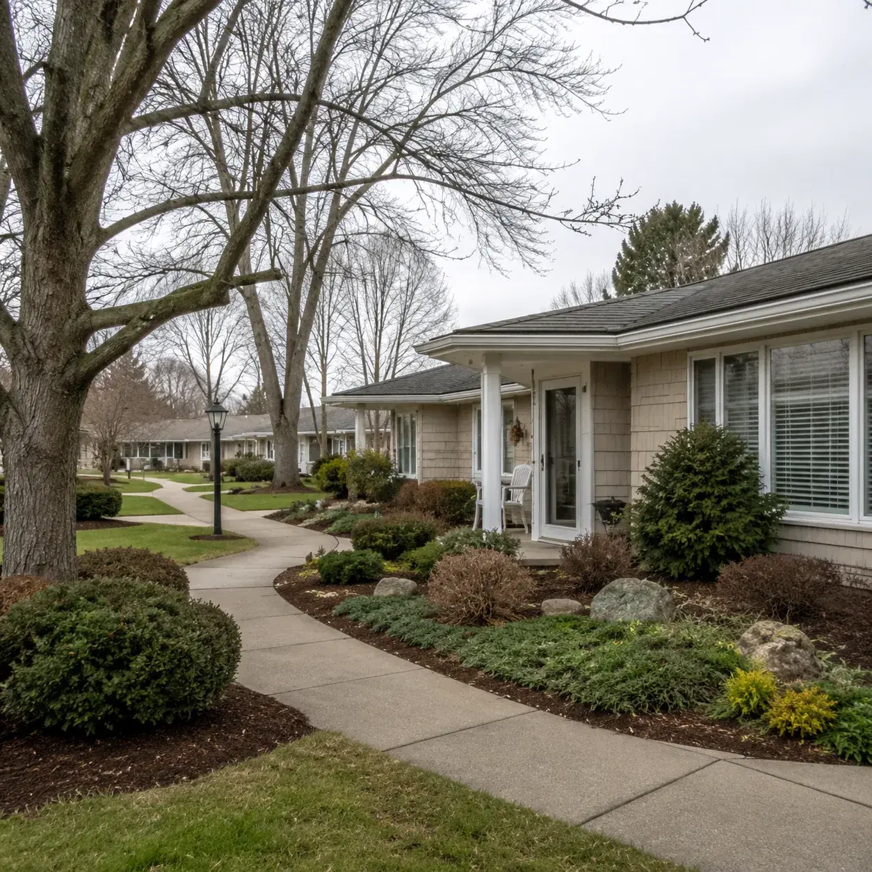 Realistic editorial photo of an older Suffolk County retirement condo village with low buildings, mature trees, sidewalk