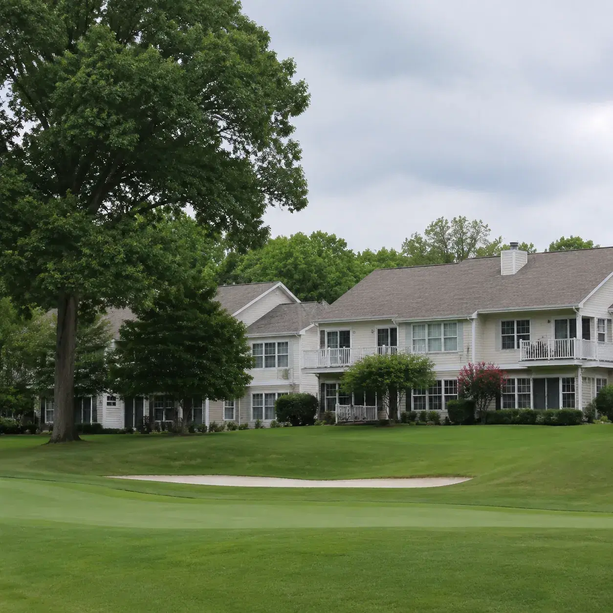 Realistic editorial photo of a New Jersey 55 plus golf community with low condos, fairway grass, trees, and gray afterno