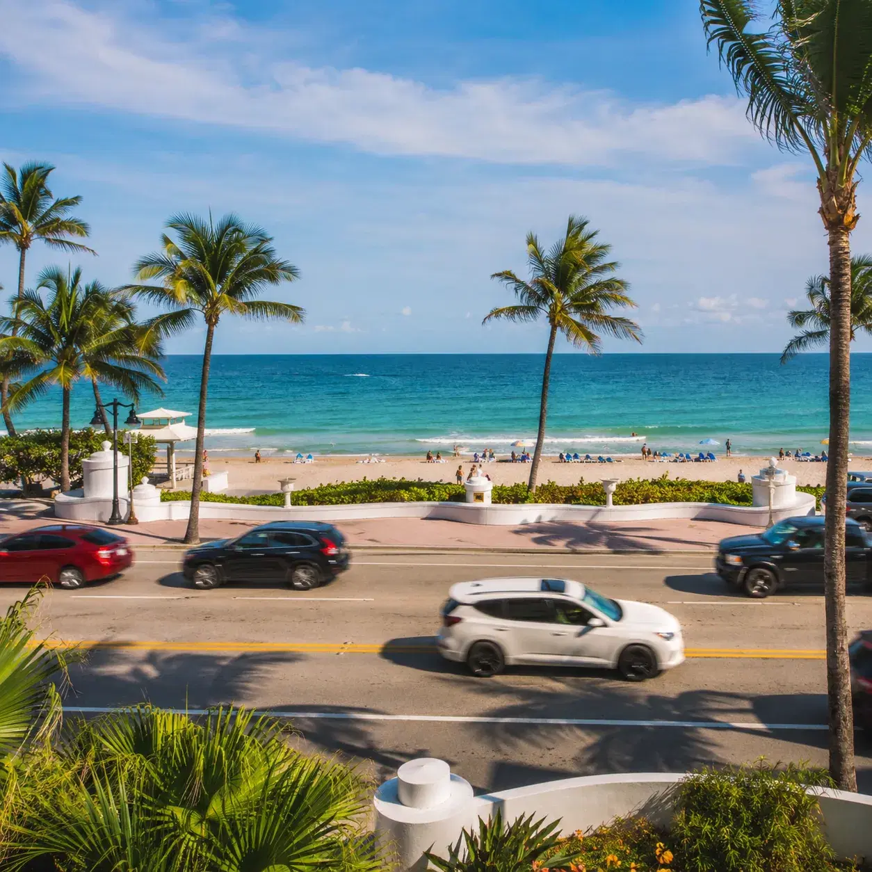 Realistic editorial photo of Florida beach vacation scene showing oceanfront rates across a busy road, bright coastal se