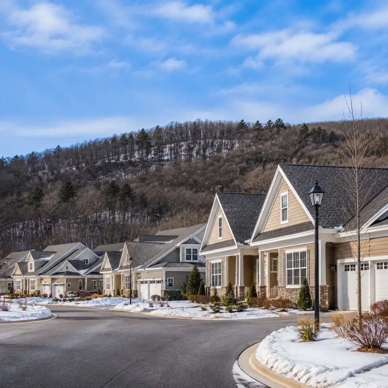 Realistic editorial photo of a Hudson Valley active adult community with townhomes, wooded hills, a cold blue sky, and s