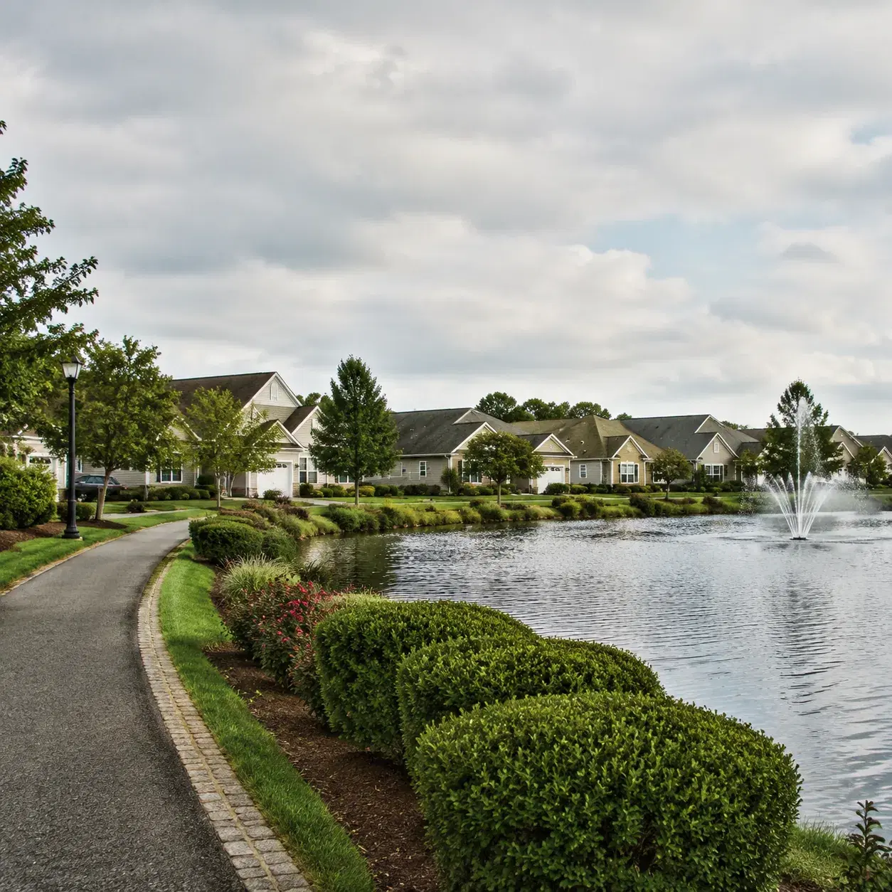Realistic editorial photo of a Jackson New Jersey 55 plus neighborhood with attached homes, a small lake, a walking path