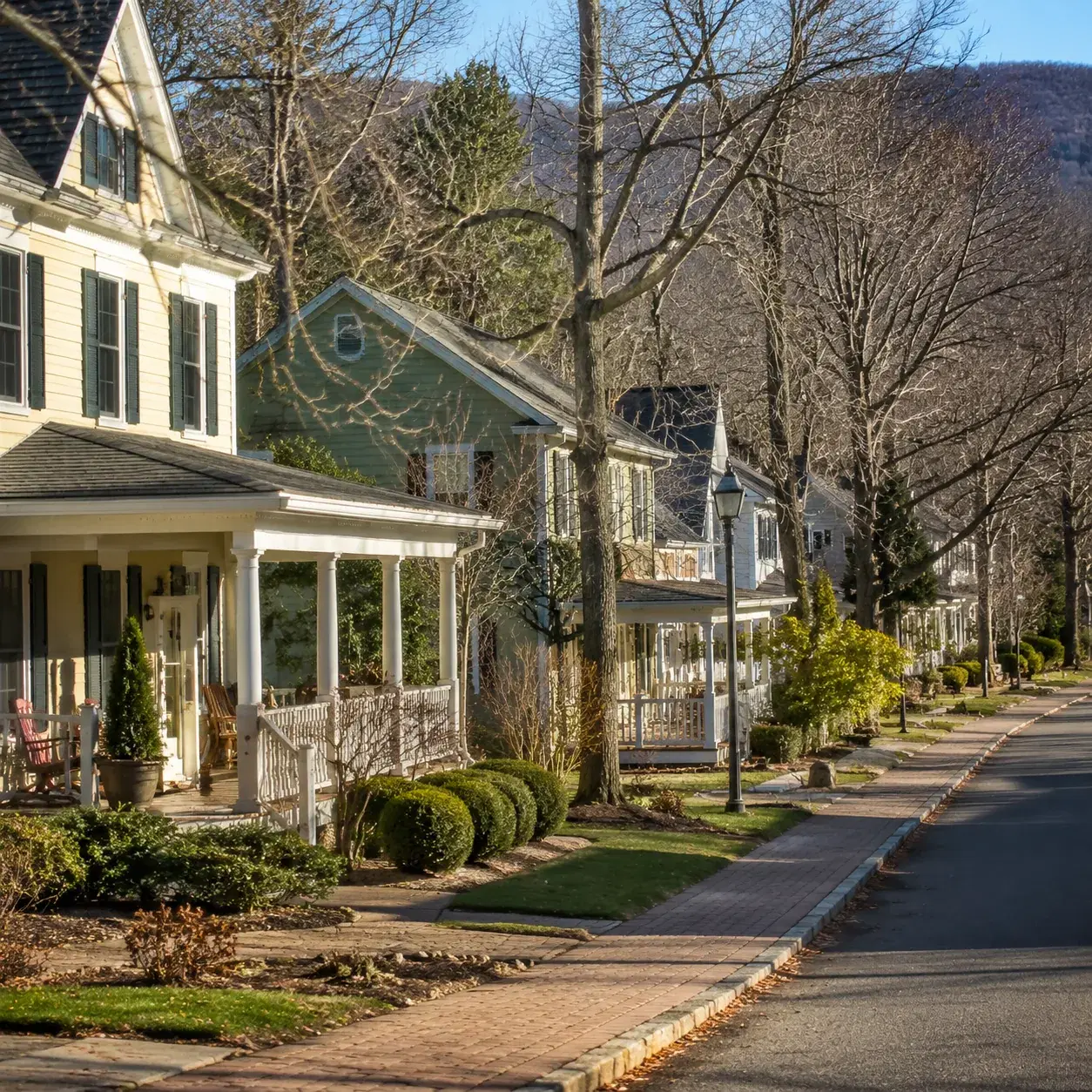 Realistic editorial photo of a charming Hudson Valley 55 plus neighborhood with front porches, village-style streets, ba