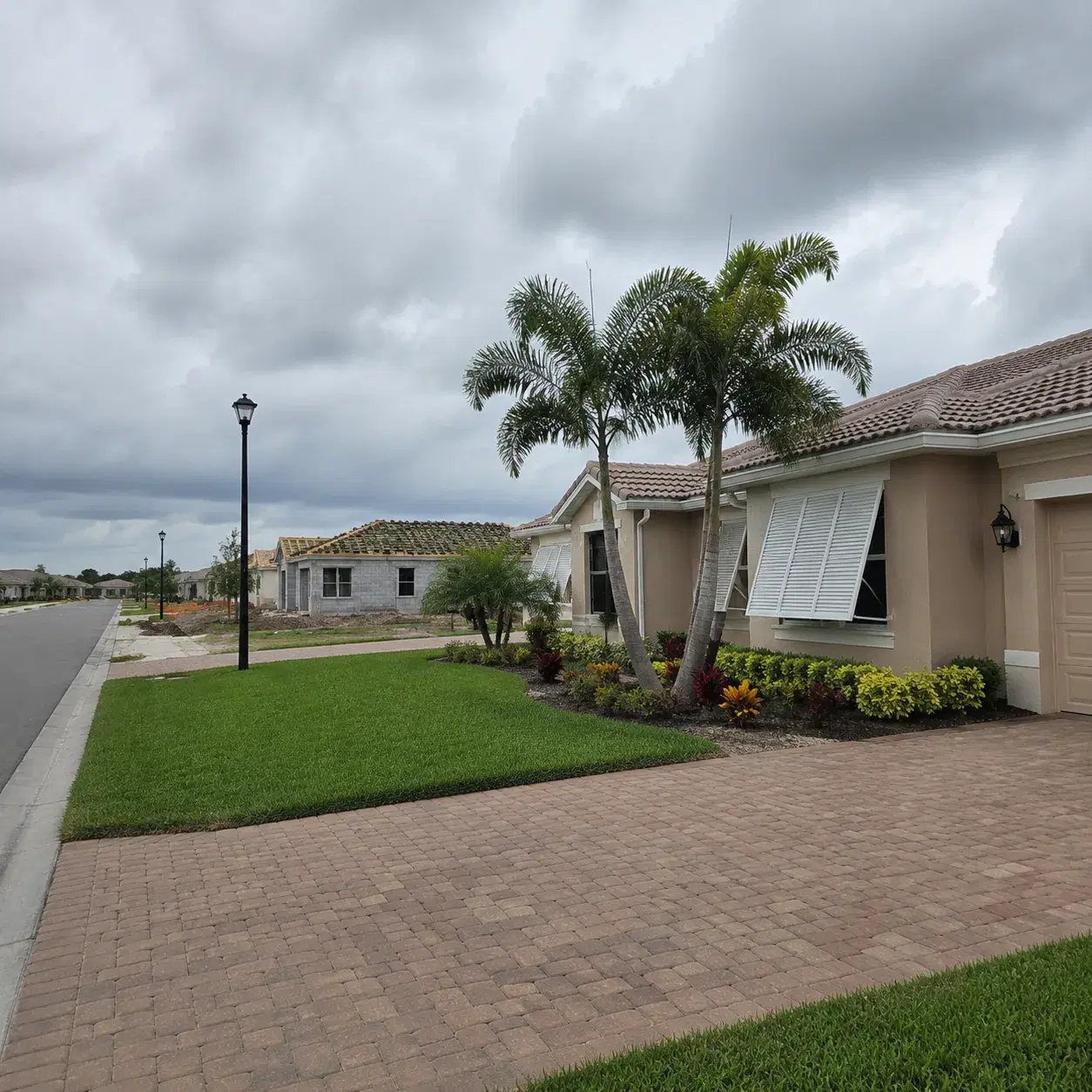 Realistic editorial photo of a Port St. Lucie 55 plus community with new construction nearby, storm shutters, tidy lawns