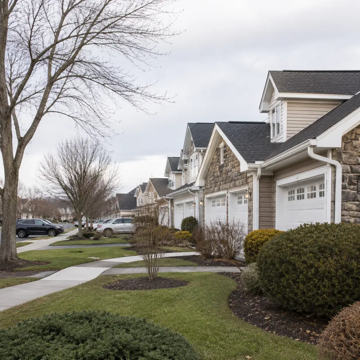 Realistic editorial photo of a Freehold New Jersey active adult neighborhood with attached homes, bare trees, parked car