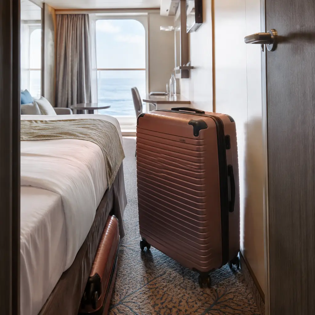open cruise cabin with one suitcase sliding neatly under the bed and another oversized matching case blocking the walkwa