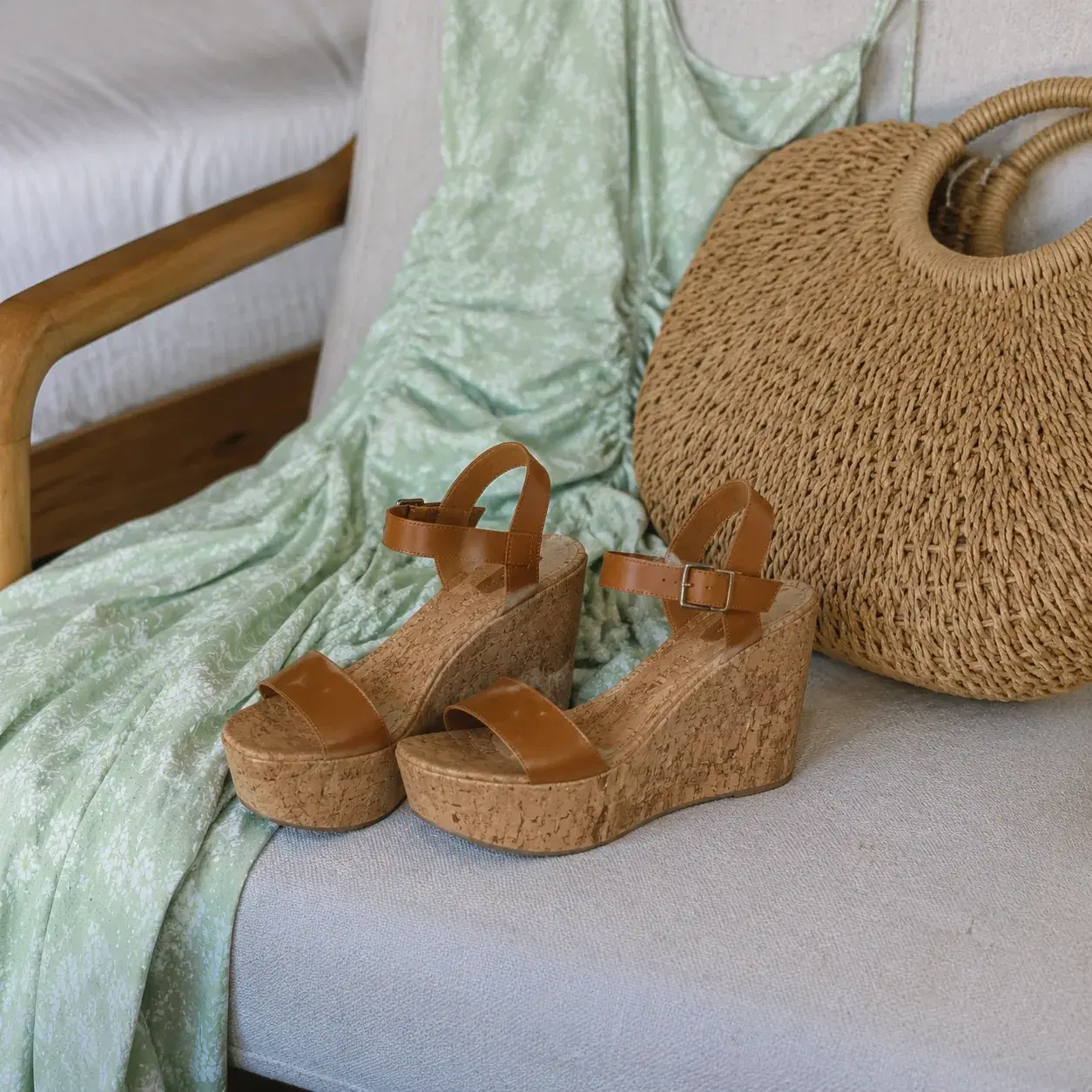 Realistic editorial photo of cork wedge sandals beside a summer dress and woven tote on a bedroom chair, visible cork pl