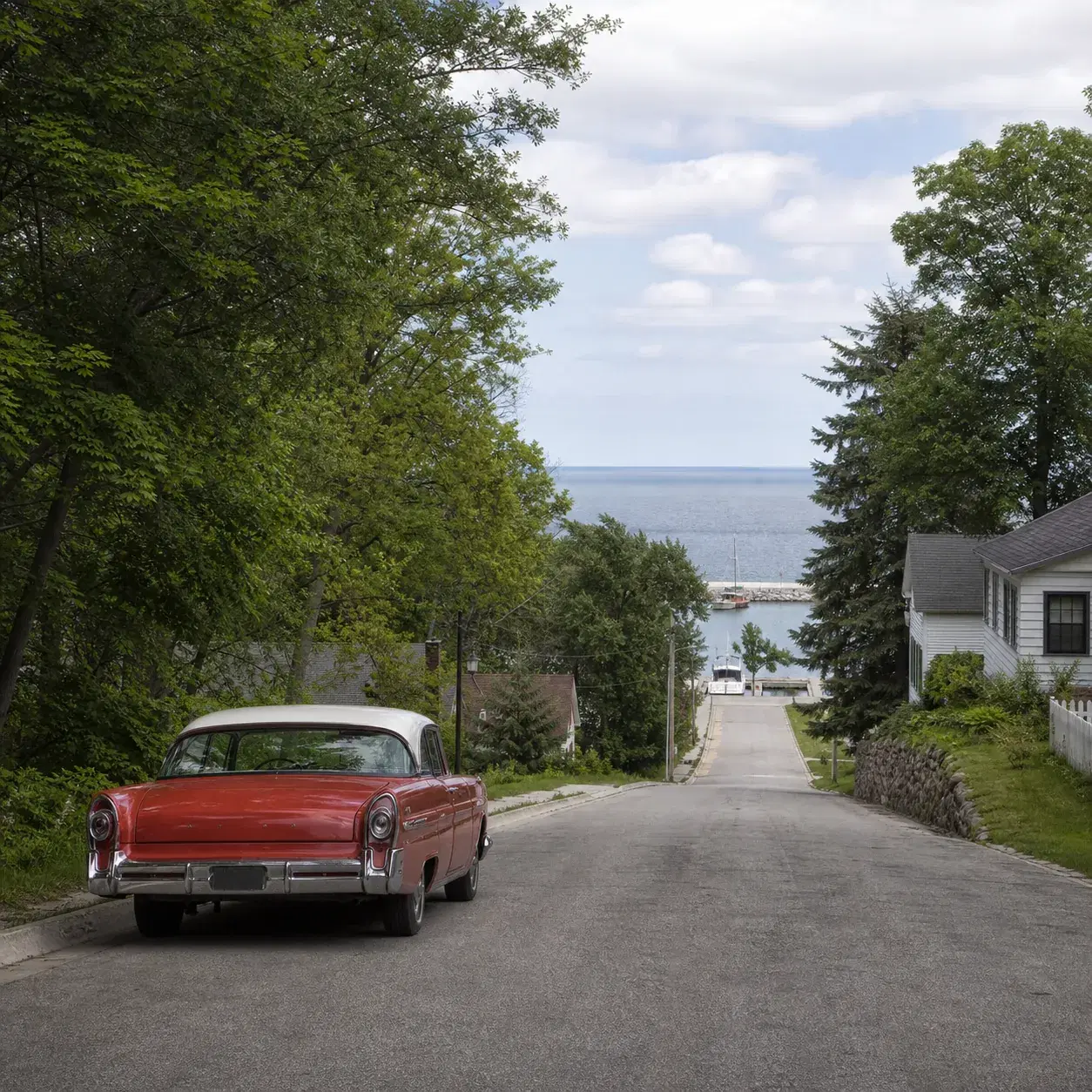 Realistic editorial photo of a quiet Wisconsin coastal road with lake water glimpsed through trees, a small harbor, and 