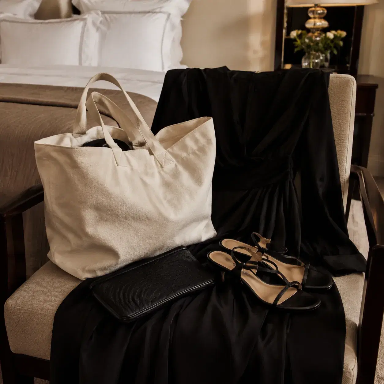 Realistic editorial photo of a large casual canvas tote placed beside an elegant black evening outfit and low heels on a