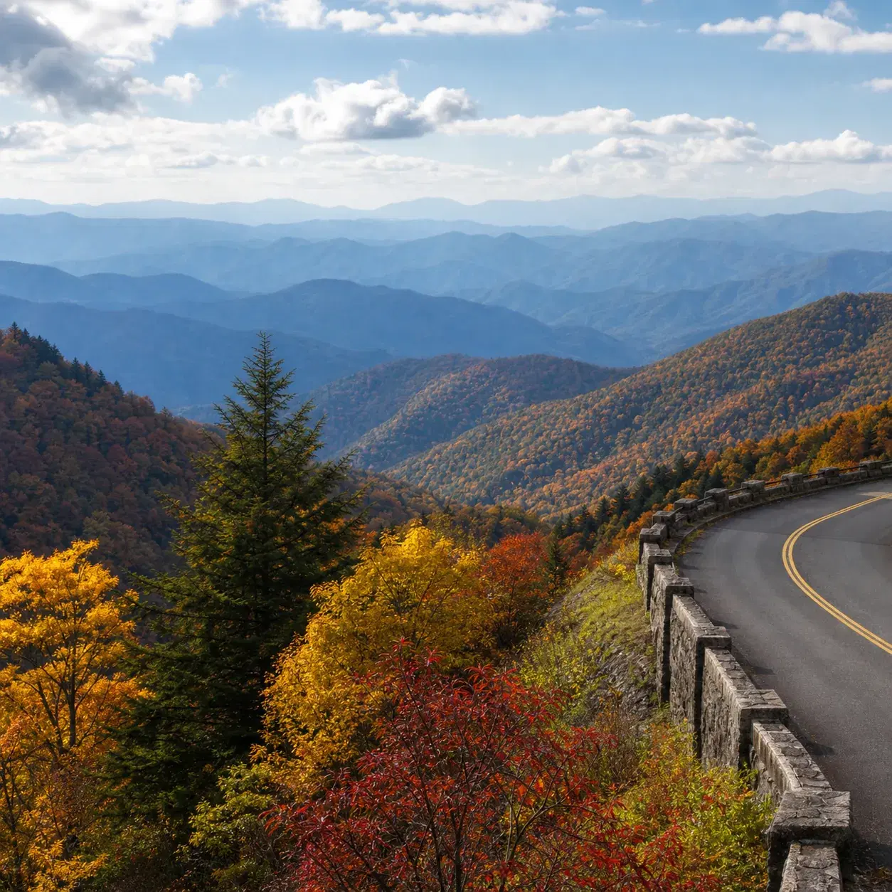 Realistic editorial photo of a mountain road in Great Smoky Mountains National Park with layered blue ridges, fall color