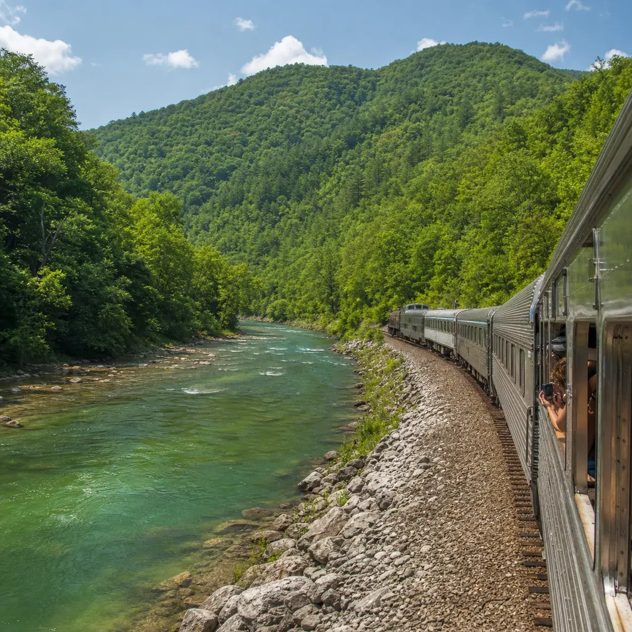 Realistic editorial photo of a scenic train curving along the Nantahala River in North Carolina with forested Smoky Moun