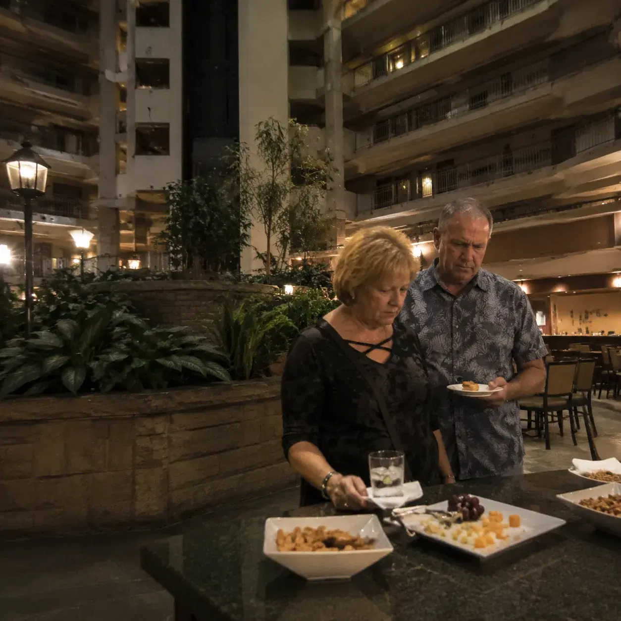 Embassy Suites atrium hotel interior showing tired landscaping, dim lighting, empty manager's reception area with limite