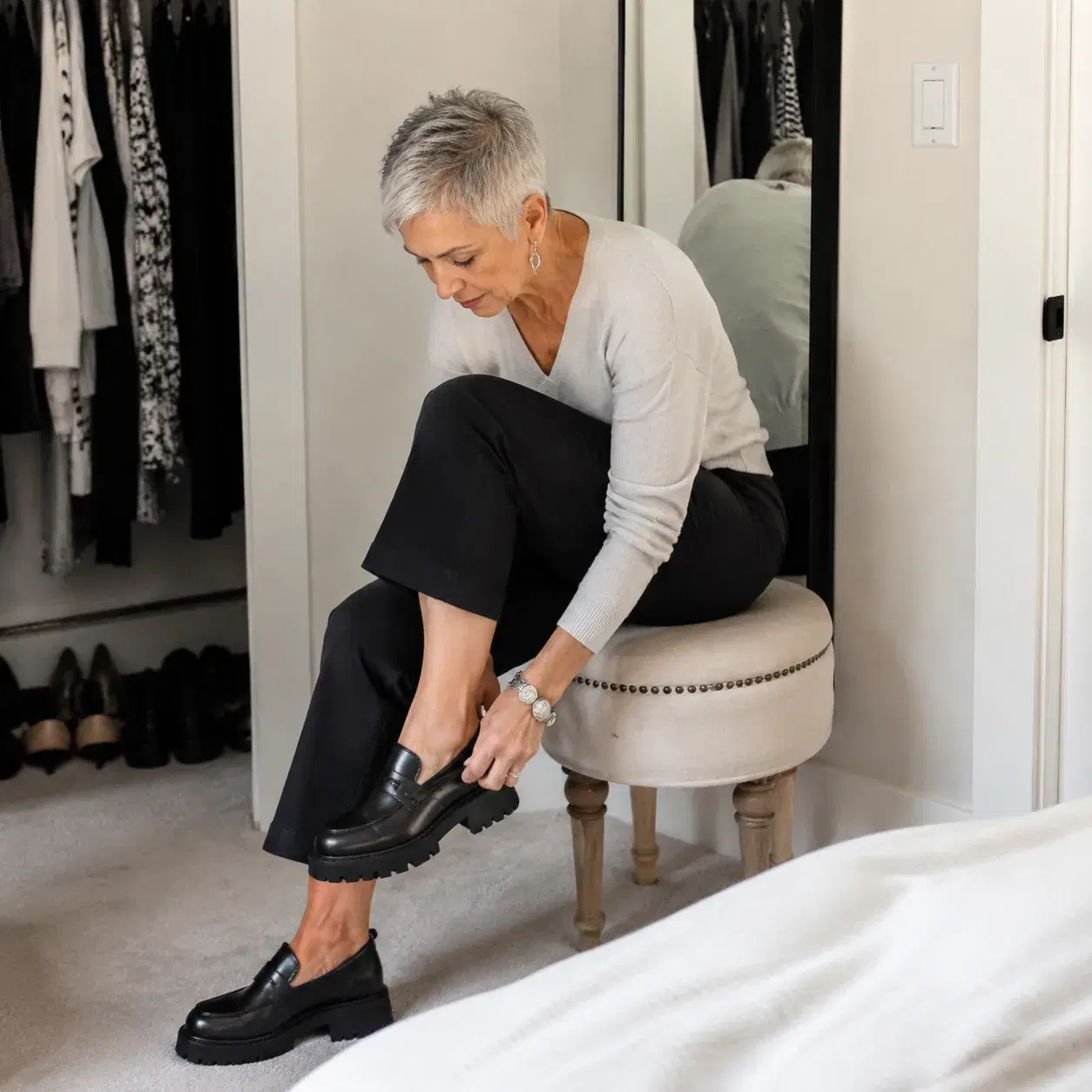 Realistic editorial photo of a woman over 50 in a short severe haircut trying on heavy shoes with cropped pants near a c