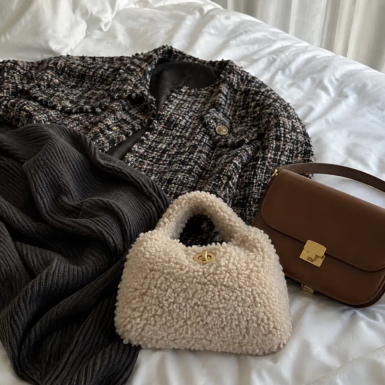 Realistic editorial photo of a fuzzy textured handbag beside a busy tweed jacket, ribbed knit, and smoother leather bag