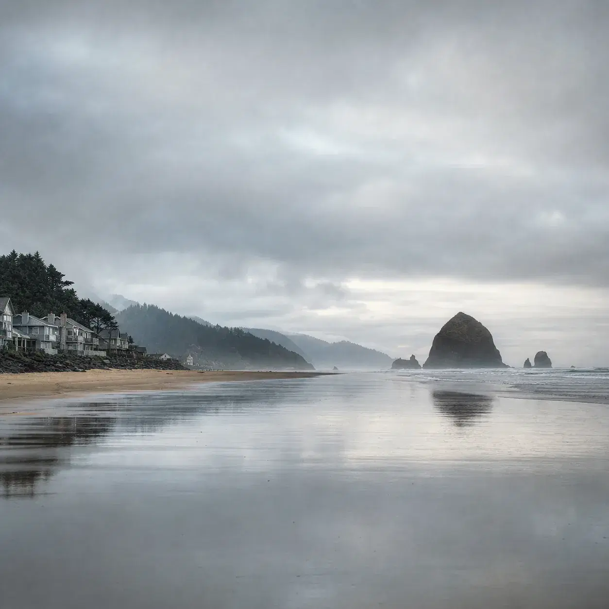 Realistic editorial photo of Cannon Beach Oregon with Haystack Rock in the distance, wet sand reflections, small coastal