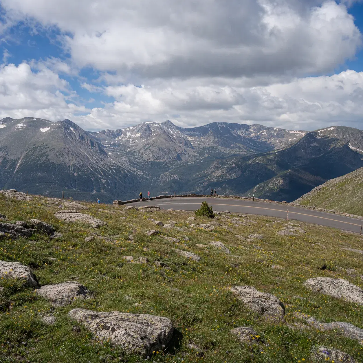 Realistic editorial photo of Trail Ridge Road above treeline in Rocky Mountain National Park with tundra, distant peaks,