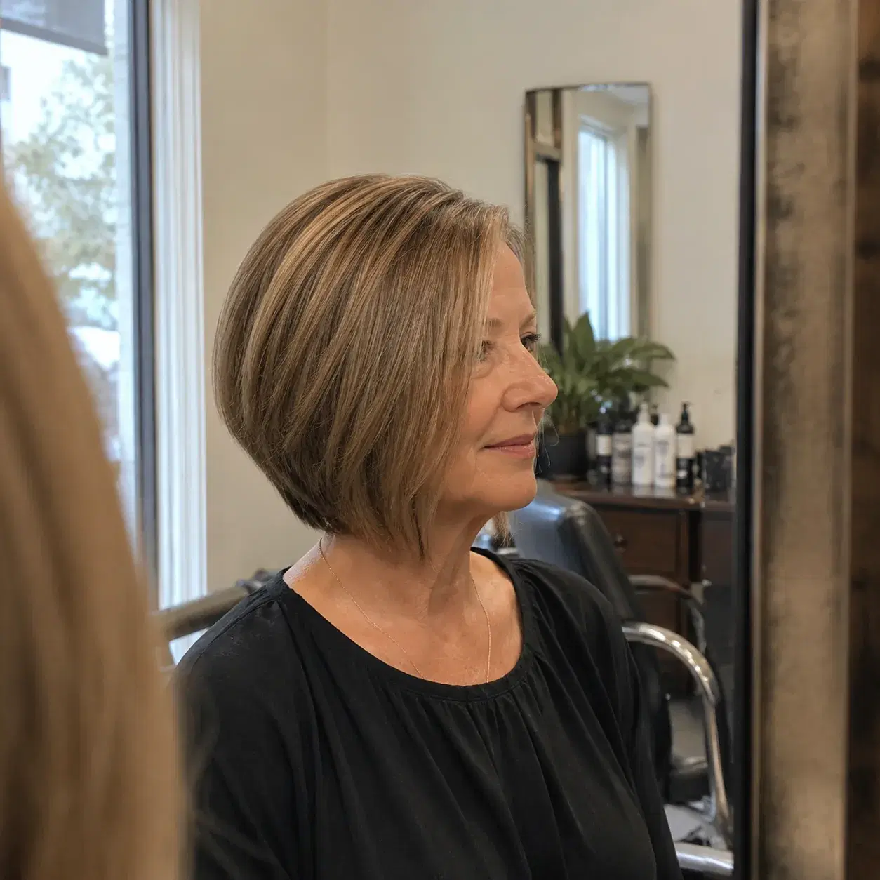 Realistic editorial photo of a woman over 50 with a slightly angled bob longer in front, side view in salon mirror, soft