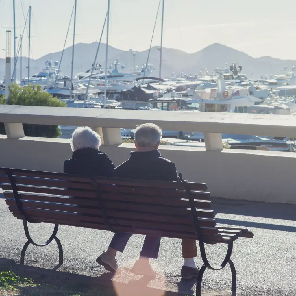 Older couple resting on a bench beside a marina in Cannes