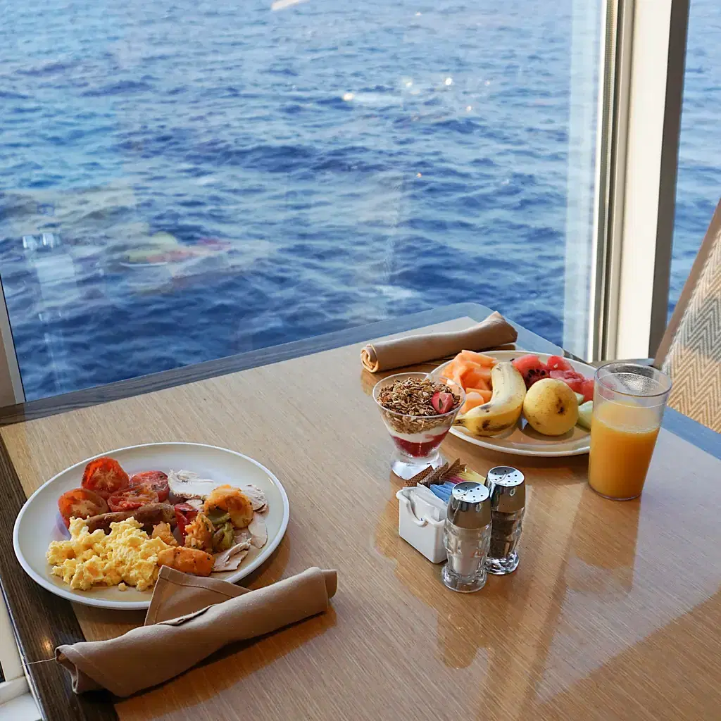 Breakfast table beside a cruise ship window overlooking the sea