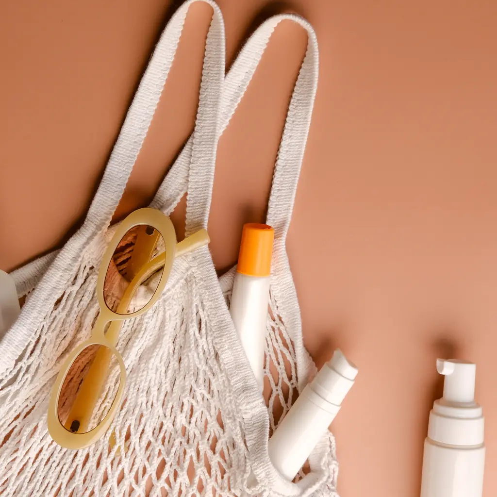 Sunscreen bottles and sunglasses packed in a mesh beach bag