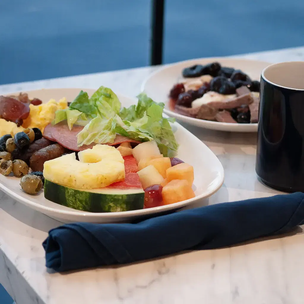 A breakfast plate with fruit and salad beside a cruise ship window