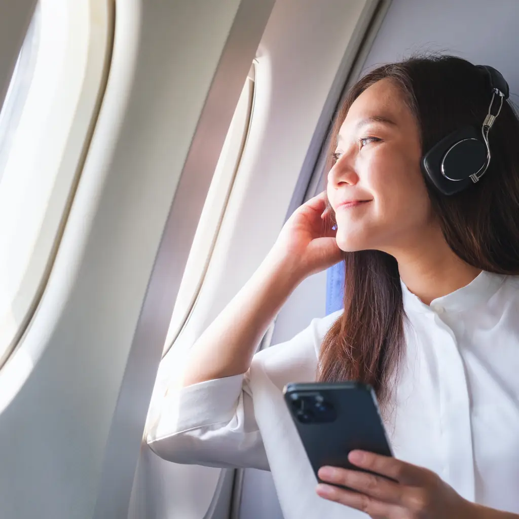 A passenger wearing over-ear headphones beside an aircraft window