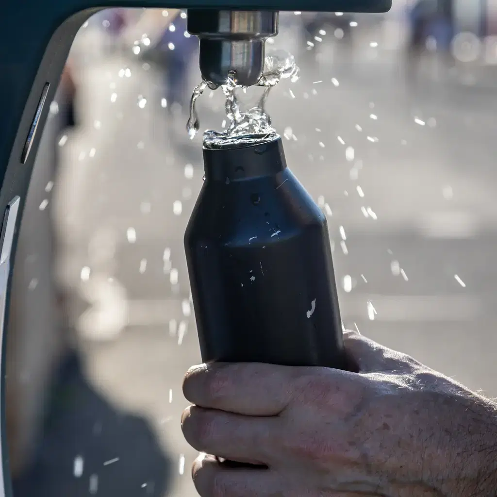 A reusable water bottle being filled at a drinking-water tap