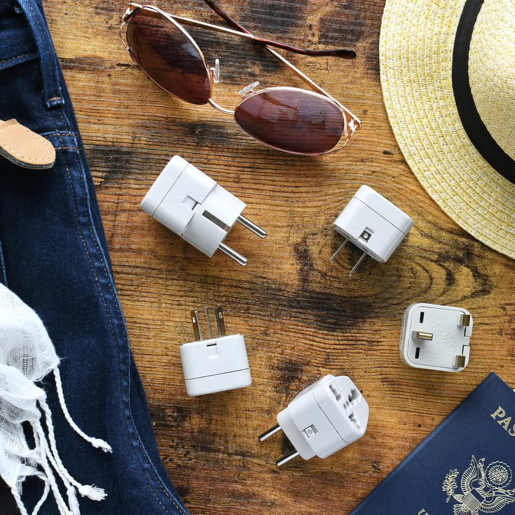 Travel plug adapters arranged with a passport, hat and sunglasses