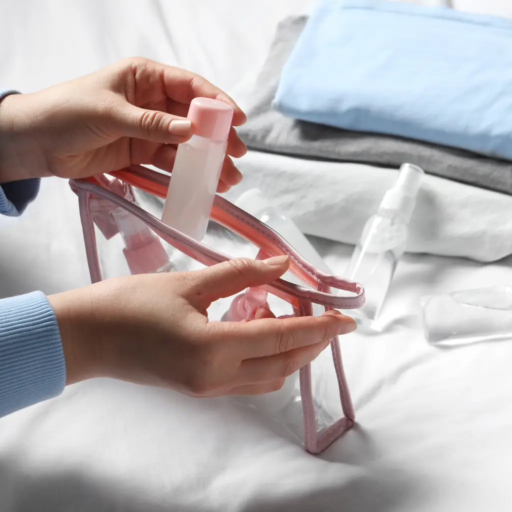 Small toiletry bottles being packed into a clear travel pouch
