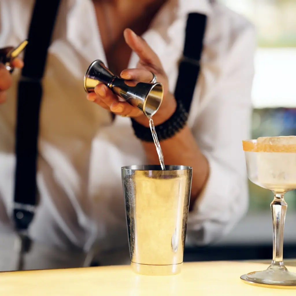 A bartender measuring a drink with a jigger
