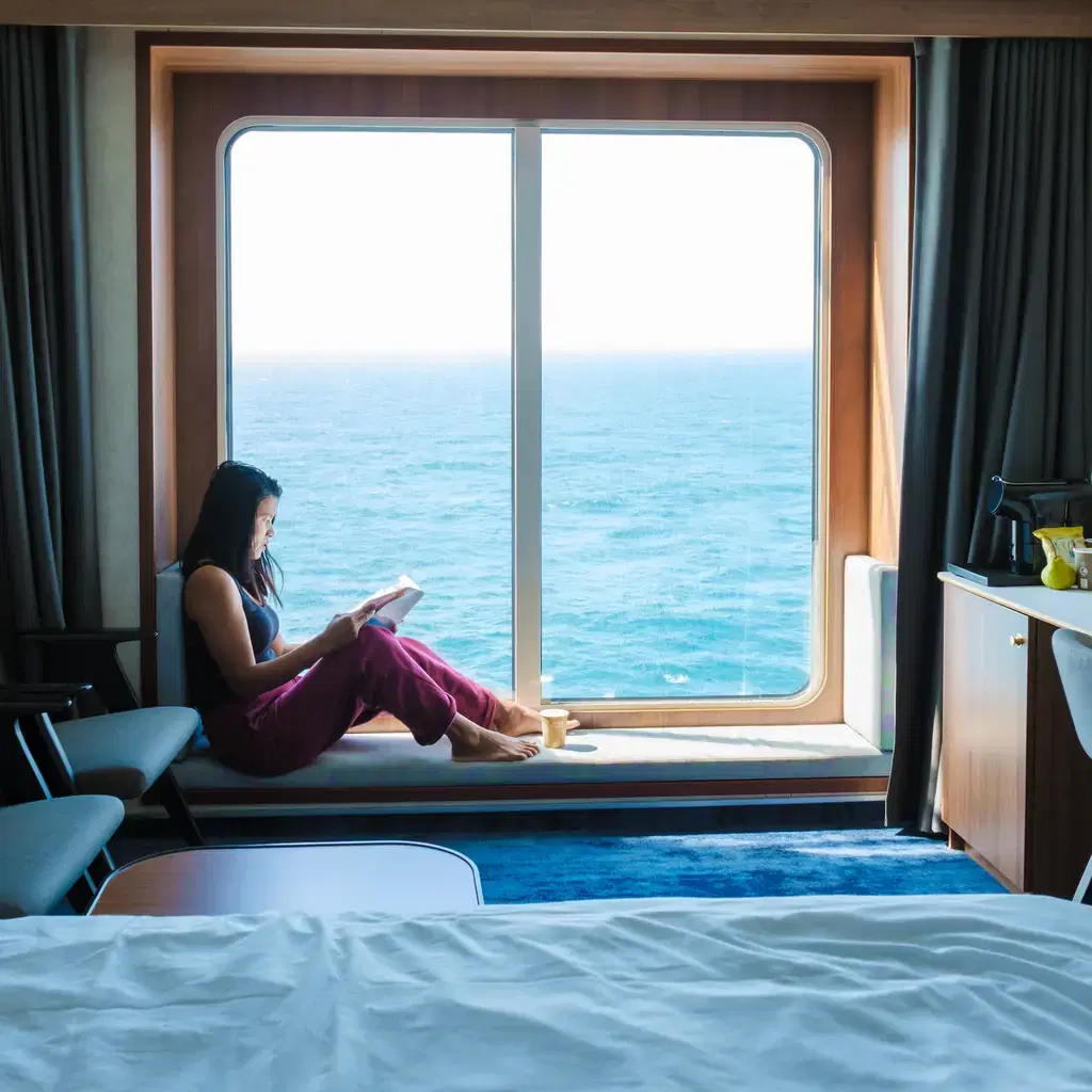 A woman reading beside a large cruise-cabin window