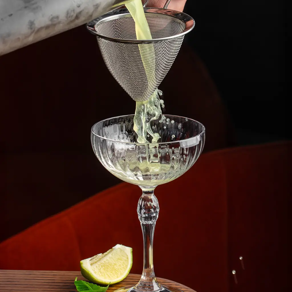 A bartender pouring a lime cocktail through a strainer