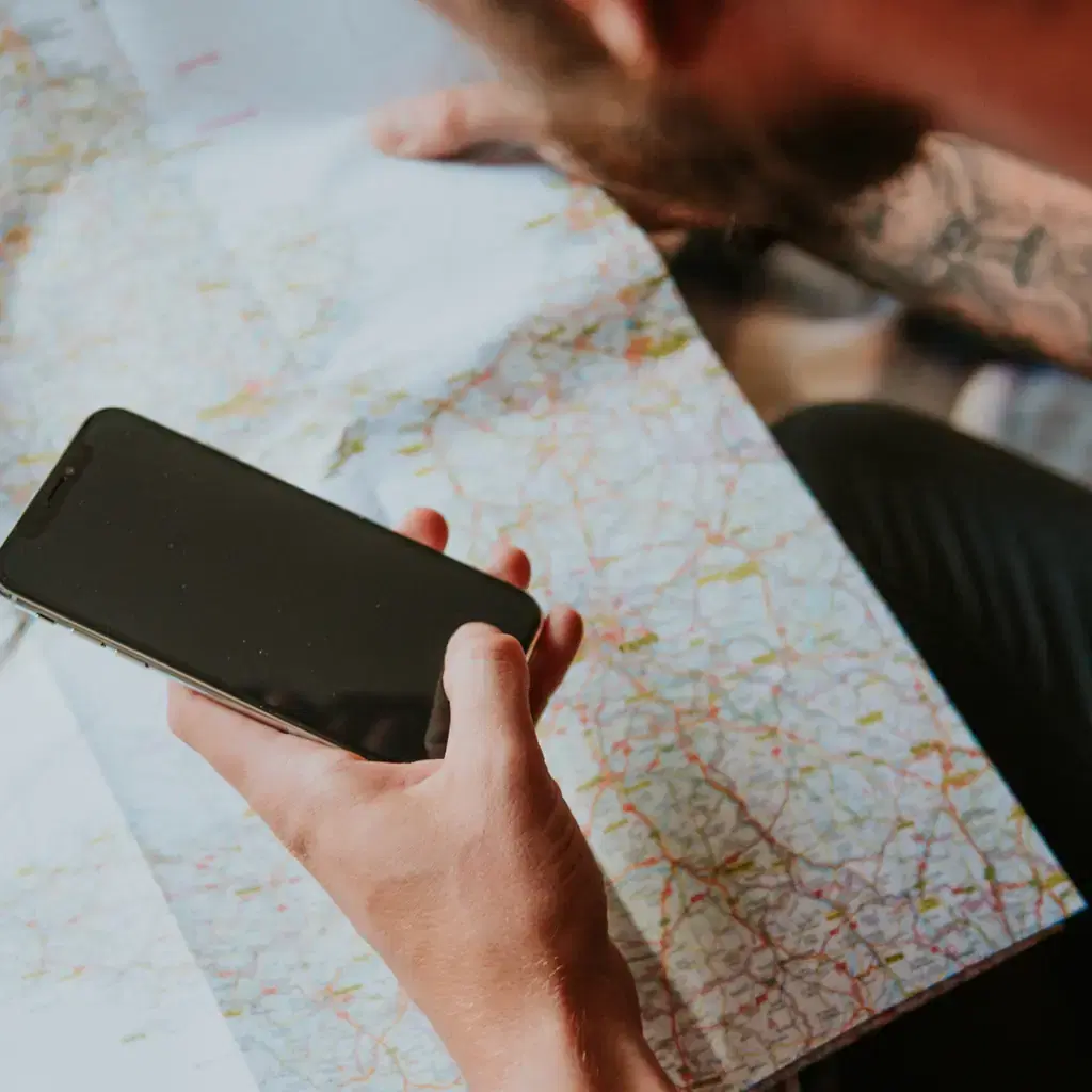A traveler checking a smartphone beside a paper map