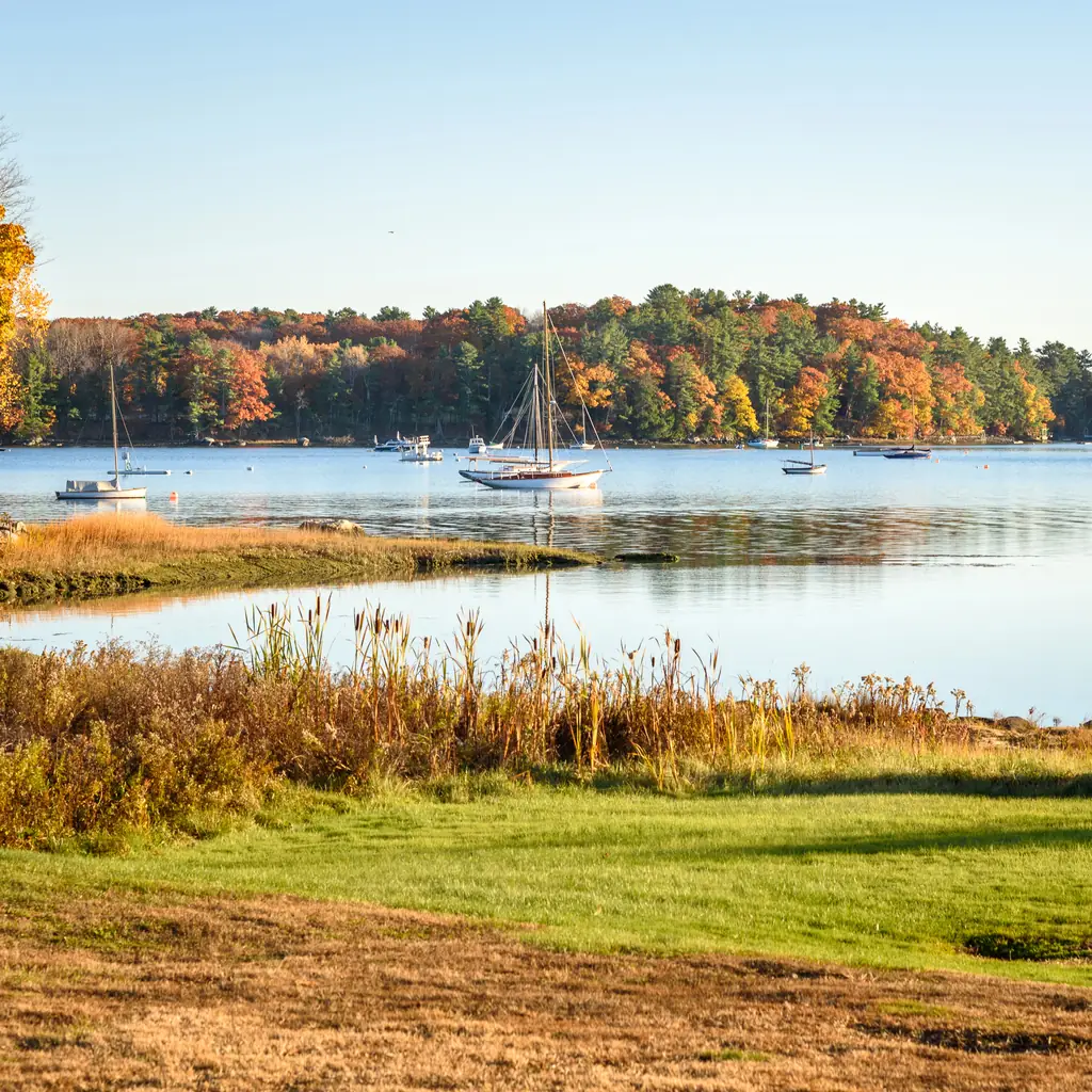 A boat moored by an autumn shoreline in Damariscotta, Maine.