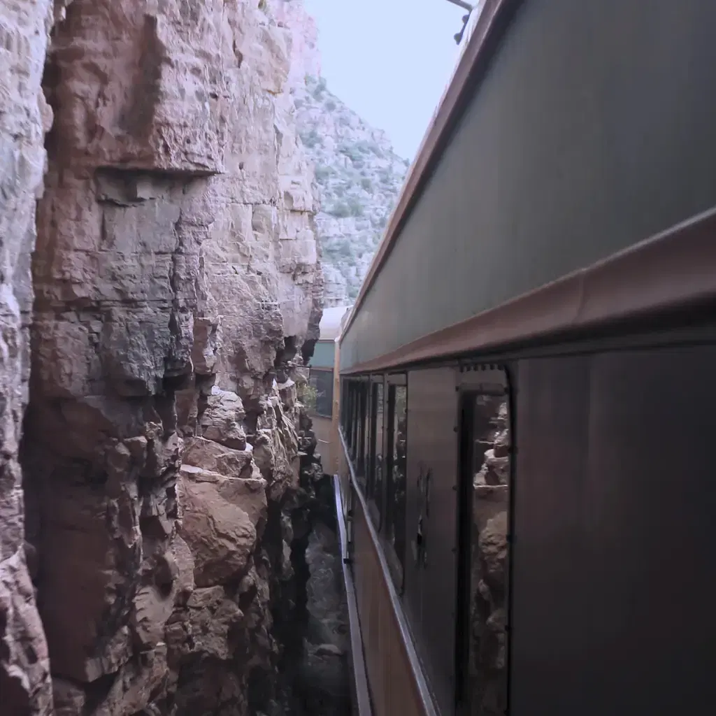 A passenger train passes beside a red-rock wall in Verde Canyon, Arizona.