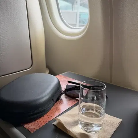 A headphone case, sunglasses and glass of water on an airplane tray table