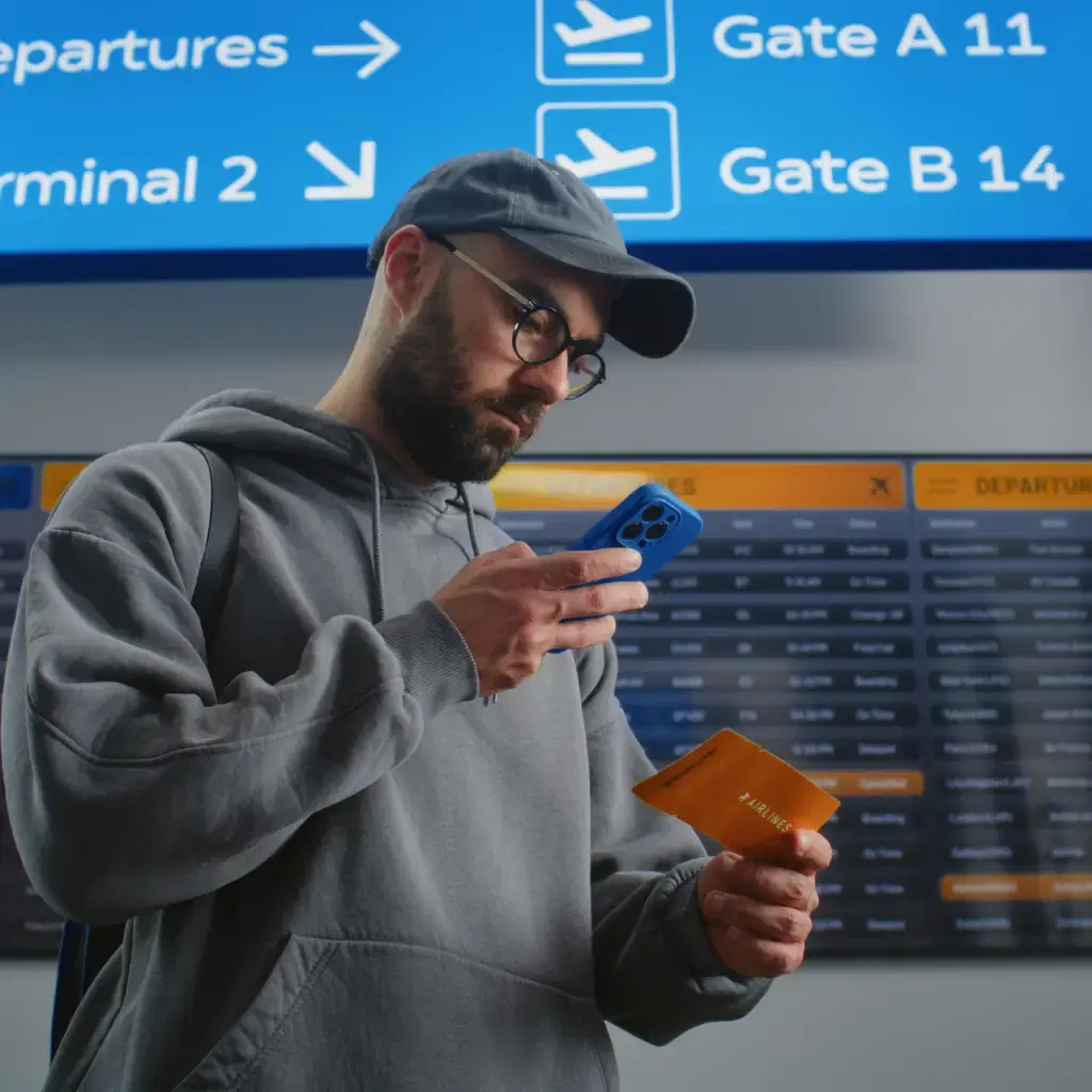 A traveler checking a phone beneath airport departure signs