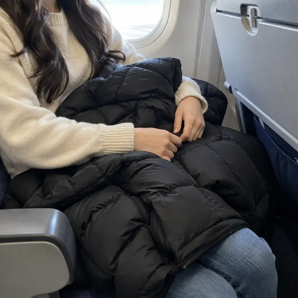 A bulky quilted puffer coat bundled on a passenger's lap in an airplane seat