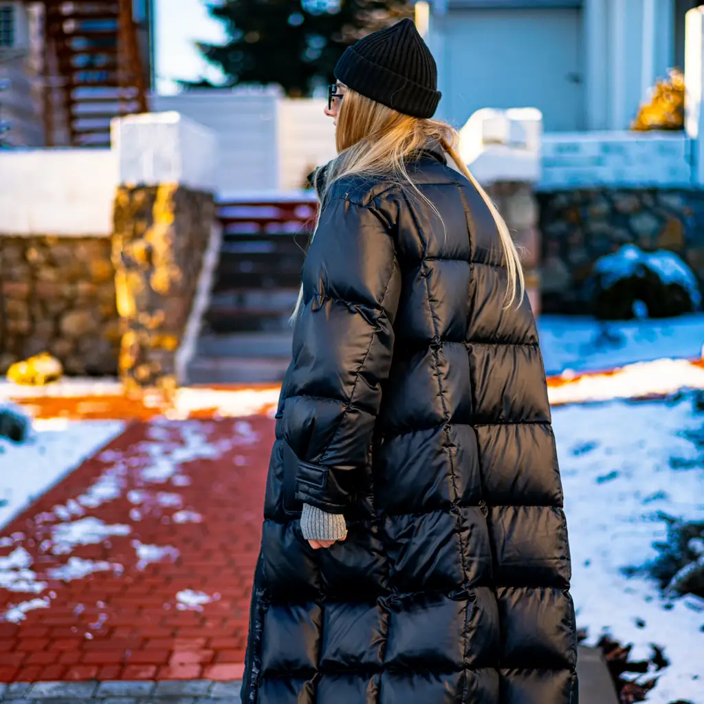 A long, shiny quilted puffer coat seen from behind on a snowy city street