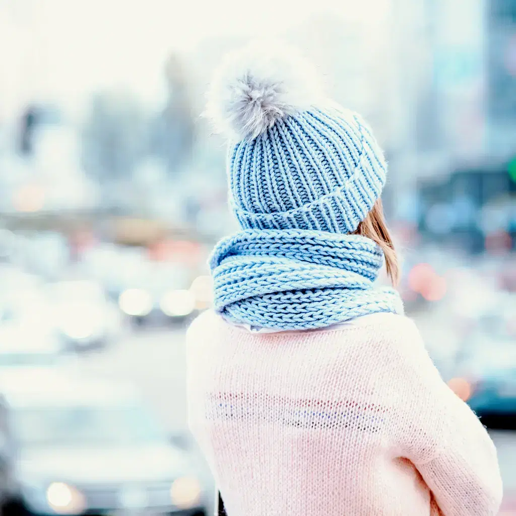 A knit beanie with a faux-fur pom-pom seen from behind on a snowy street