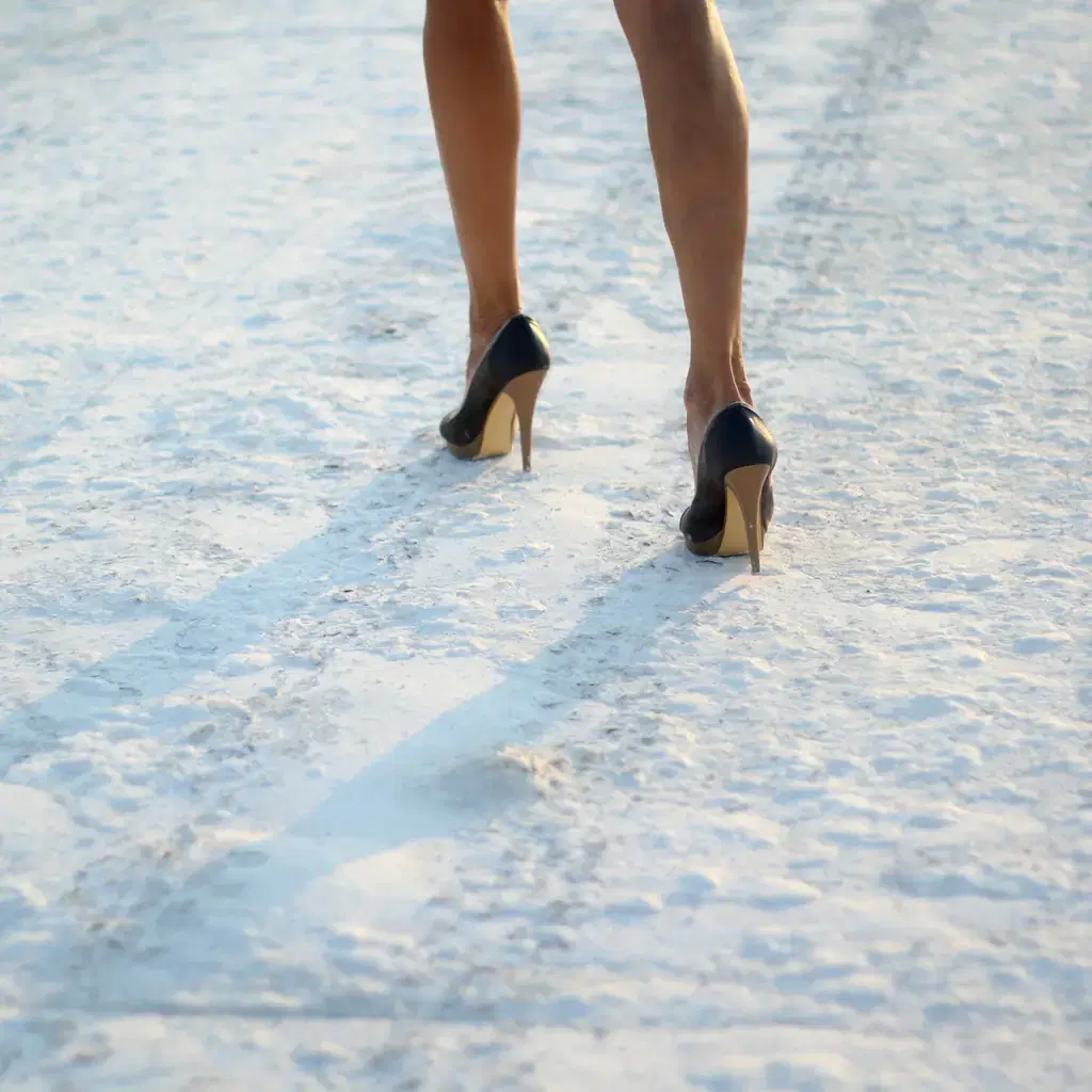 Dress flats stepping onto an icy parking lot at dusk